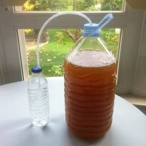 Esquema de sello de fermentación empleando otro recipiente, nótese que el extremo de la manguera en el fermentador esta cerca de la tapa mientras que el otro se encuentra sumergido en liquido