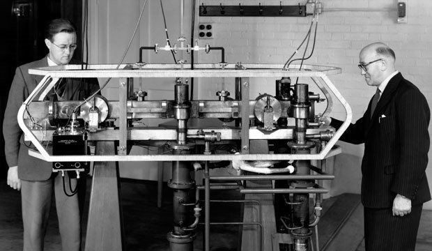 Louis Essen y J. V. L. Parry de pie junto al primer reloj atómico de cesio del mundo, desarrollado en el Laboratorio Nacional de Física del Reino Unido en 1955.