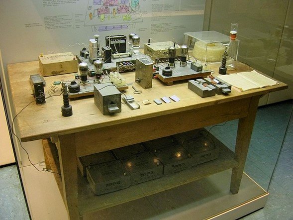 Reconstrucción del banco de pruebas utilizado para descubrir la fisión nuclear, Deutsches Museum, Múnich, con siete tubos de electrones sobre la mesa y baterías Pertrix en el estante inferior.